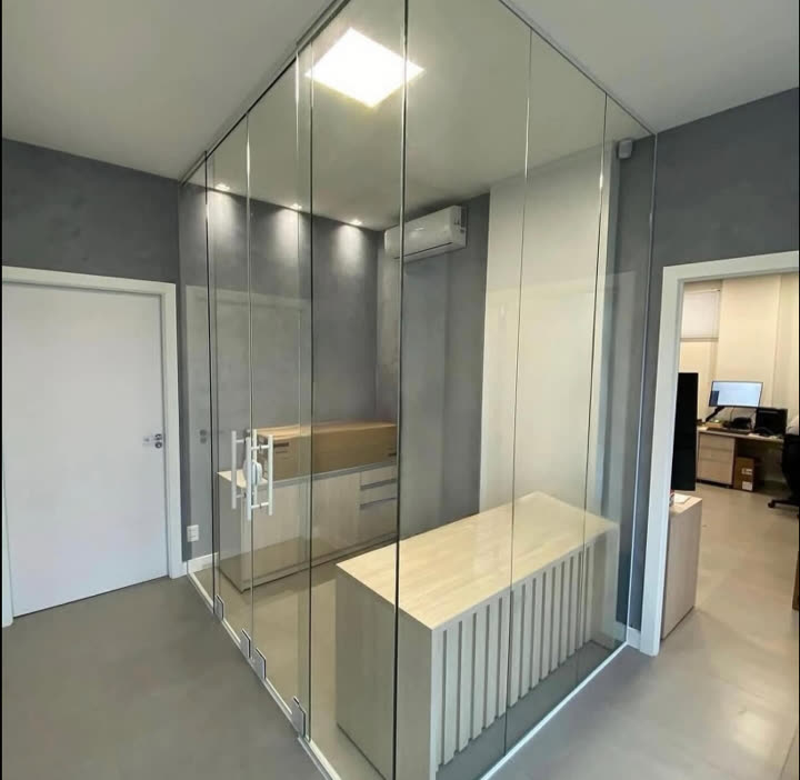Sala fechada com divisórias de vidro do piso ao teto e porta de correr, dentro de um escritório
