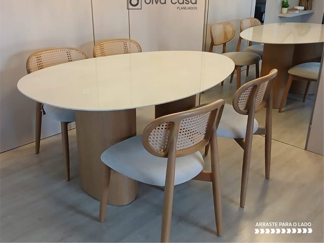 Mesa de jantar oval com tampo claro e cadeiras de palhinha com encosto arredondado