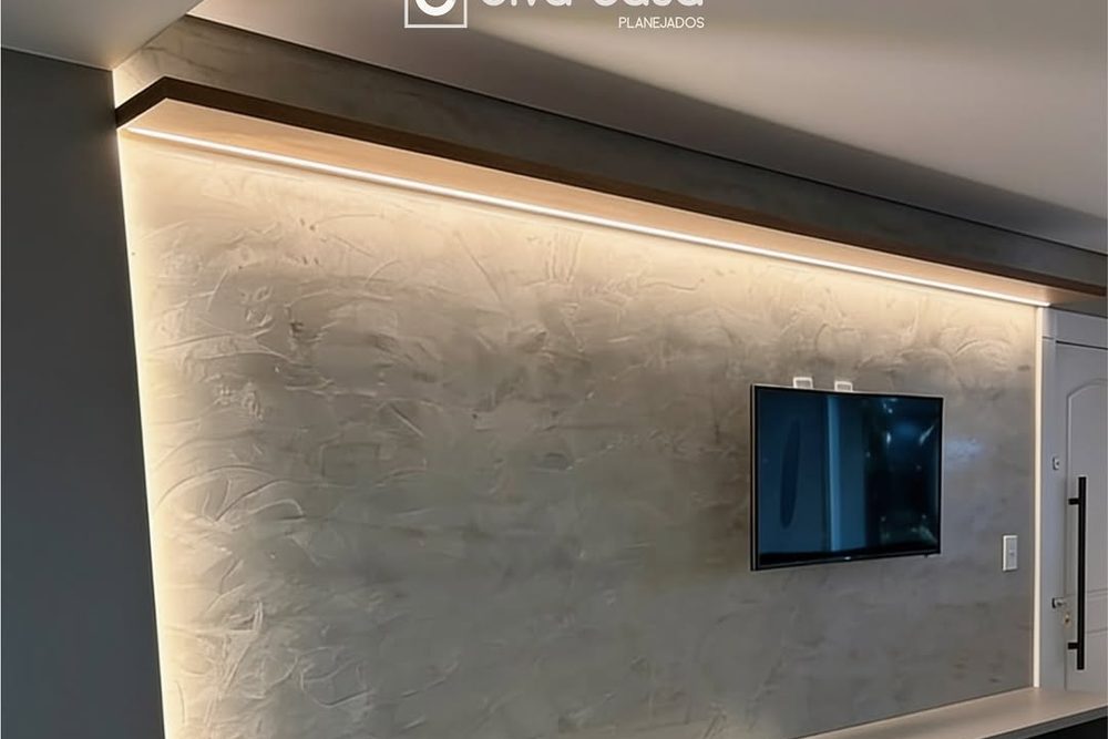 Painel de sala em tom areia com fita de LED embutida na moldura superior, TV e bancada baixa em laca fosca