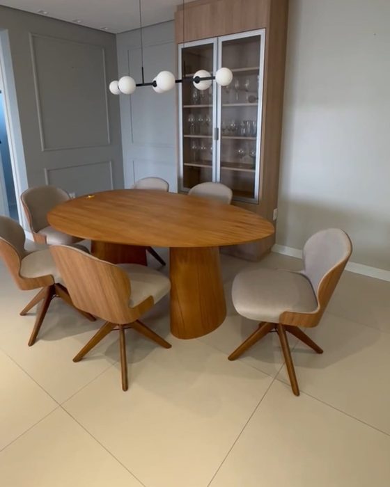 Sala de jantar com mesa redonda de madeira, cadeiras giratórias estofadas e cristaleira planejada ao fundo