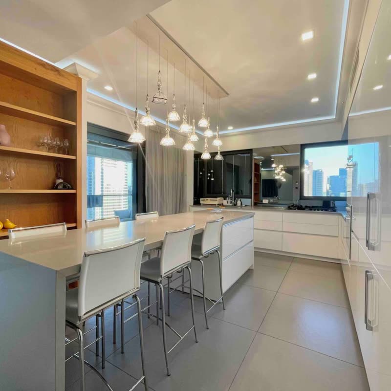 Cozinha clara de apartamento com bancada de refeições para quatro banquetas, estante de madeira com nichos e vista para a cidade pela janela