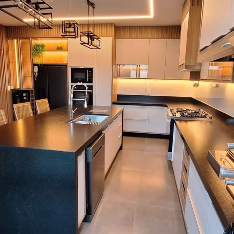 Cozinha em U com ilha central de bancada preta, armários brancos, ripado de madeira na parede e luminárias pendentes geométricas