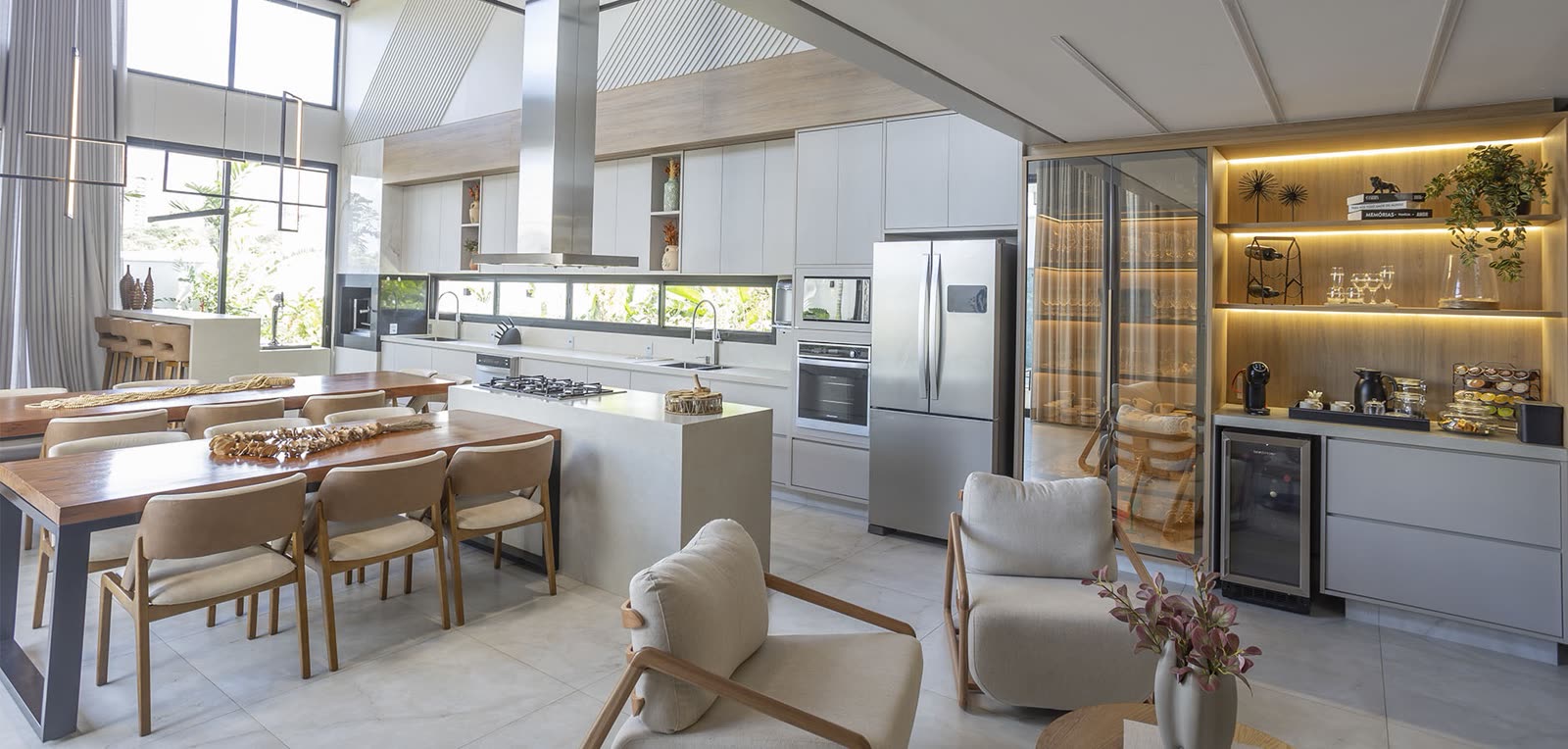 Cozinha planejada integrada à sala de jantar: ilha com bancada clara, marcenaria em madeira com iluminação embutida, adega e mesa de jantar em madeira maciça
