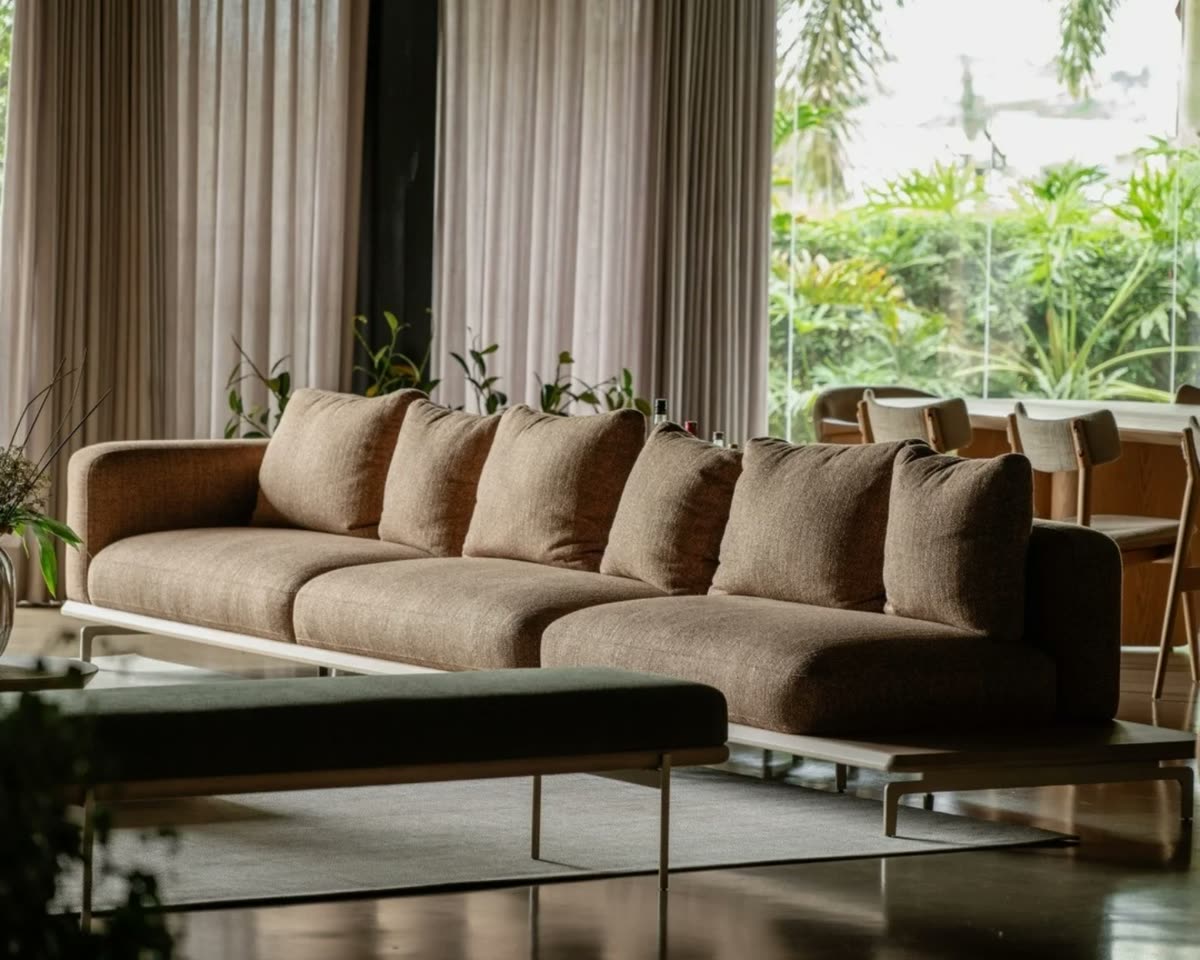 Sofá modular de linho em tom terroso numa sala integrada, com cortinas claras e vista para um jardim