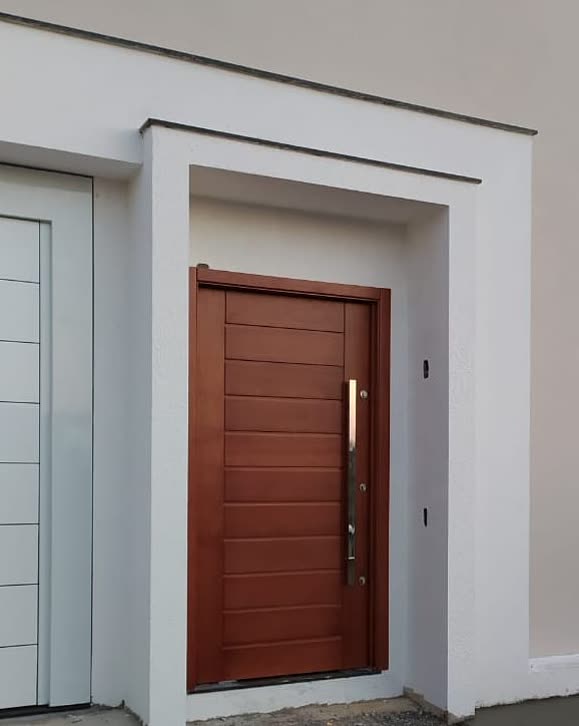 Porta de entrada de madeira com frisos horizontais e puxador em inox, em fachada branca ao lado do portão da garagem