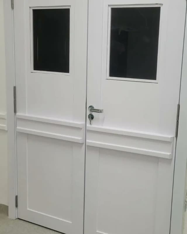 Porta dupla branca com visores de vidro e puxador cromado, instalada em corredor com rodapé alto
