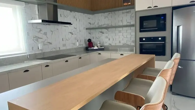 Cozinha planejada com bancada de madeira, banquetas e armários sob medida