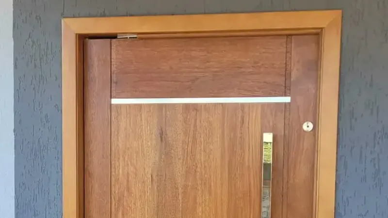 Porta de entrada em madeira maciça com puxador vertical e marco aparente